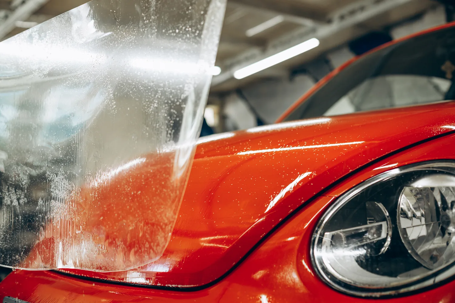 Clear paint protection film being applied to a red car hood